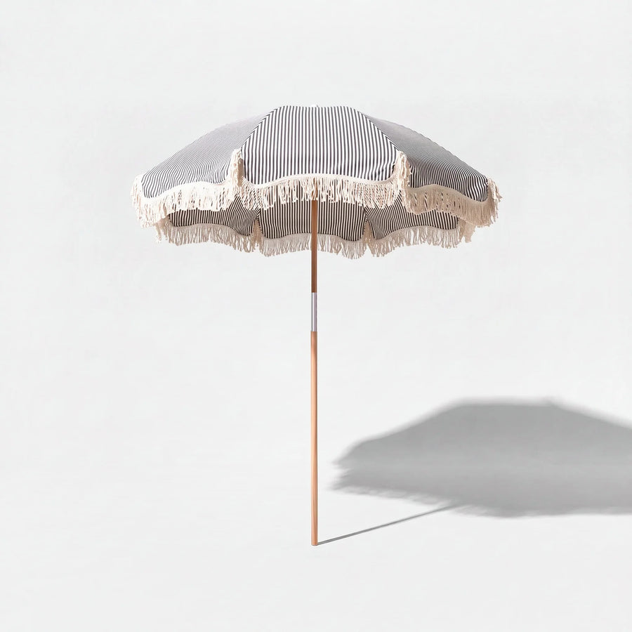 Betty's beach umbrella in dark navy and white stripe on a grey studio background with shadow