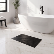 Black bamboo non slip bath mat in front of a white freestanding bath in a modern marble bathroom