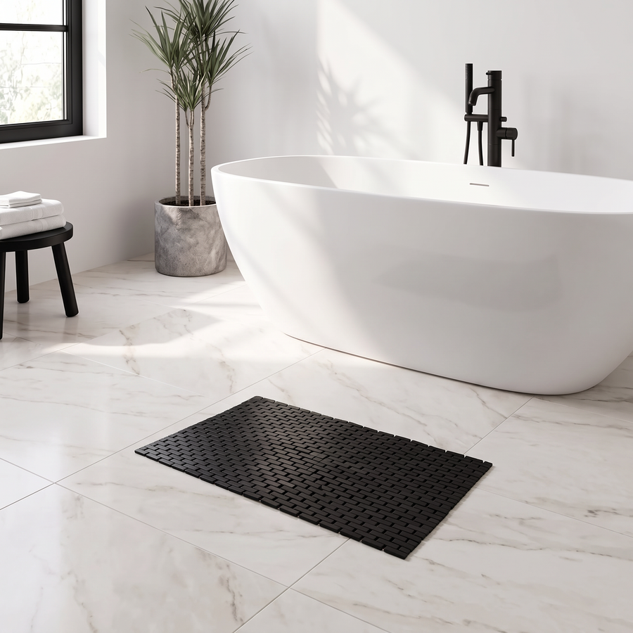 Black bamboo non slip bath mat in front of a white freestanding bath in a modern marble bathroom
