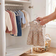 Hanging a toddler dress on a grey velvet kids hanger in a white wardrobe