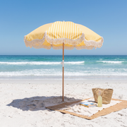 Yellow Monaco beach umbrella on a sunny beach with a rattan mat and beach bag