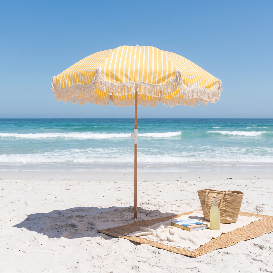 Yellow Monaco beach umbrella on a sunny beach with a rattan mat and beach bag