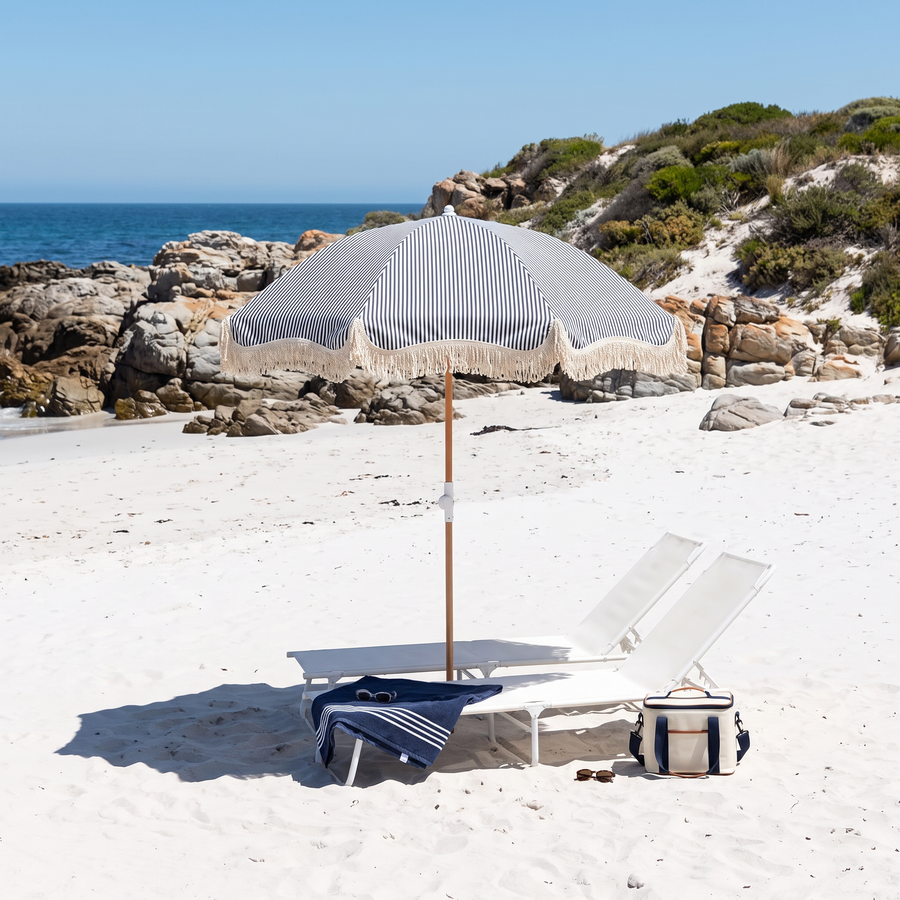 Navy Monaco beach umbrella on a white sand beach with a lounger and cooler bag