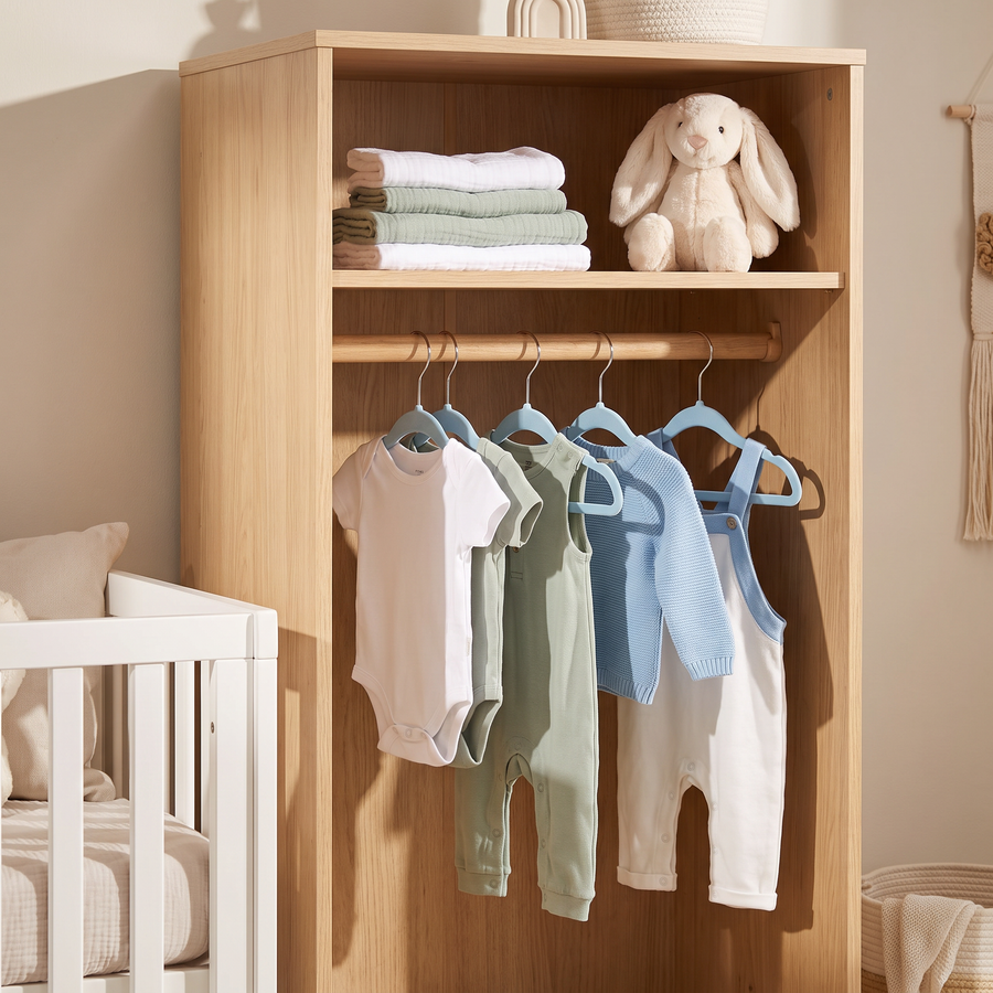 Blue velvet baby hangers with baby clothes in a modern nursery cupboard