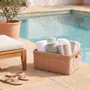 Lucy woven wicker basket with rolled towels on a pool patio