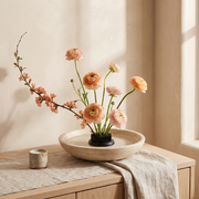 Needle Bloom flower holder in a travertine bowl with peach ranunculus