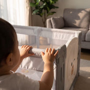 Close-up of small hands gripping the padded top rail of the play yard
